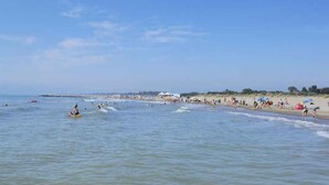 A beach with people swimming and sunbathing, a pier in the distance, and beach umbrellas.