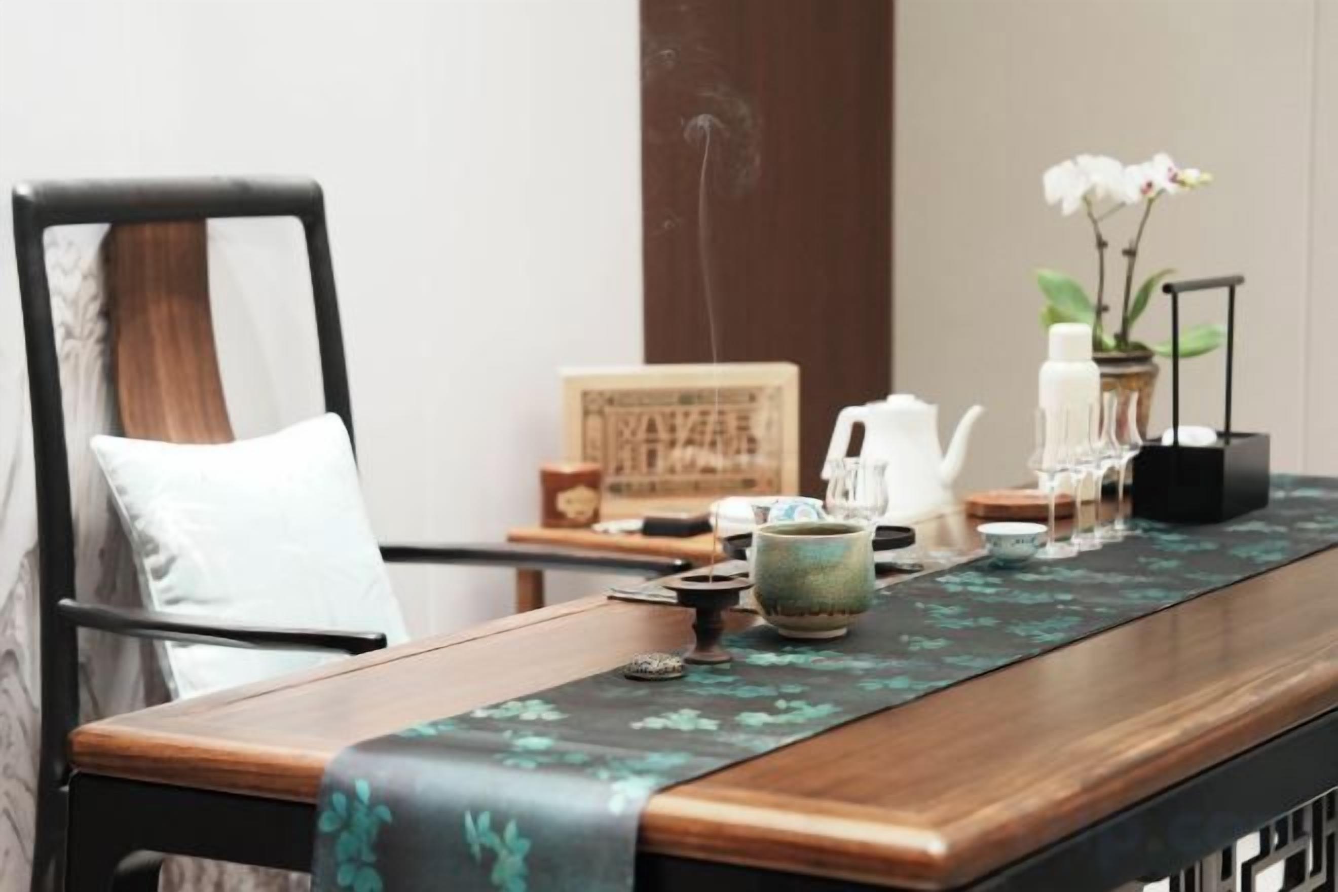 A wooden table with a green table runner, a white chair, a small potted plant, and a teapot.