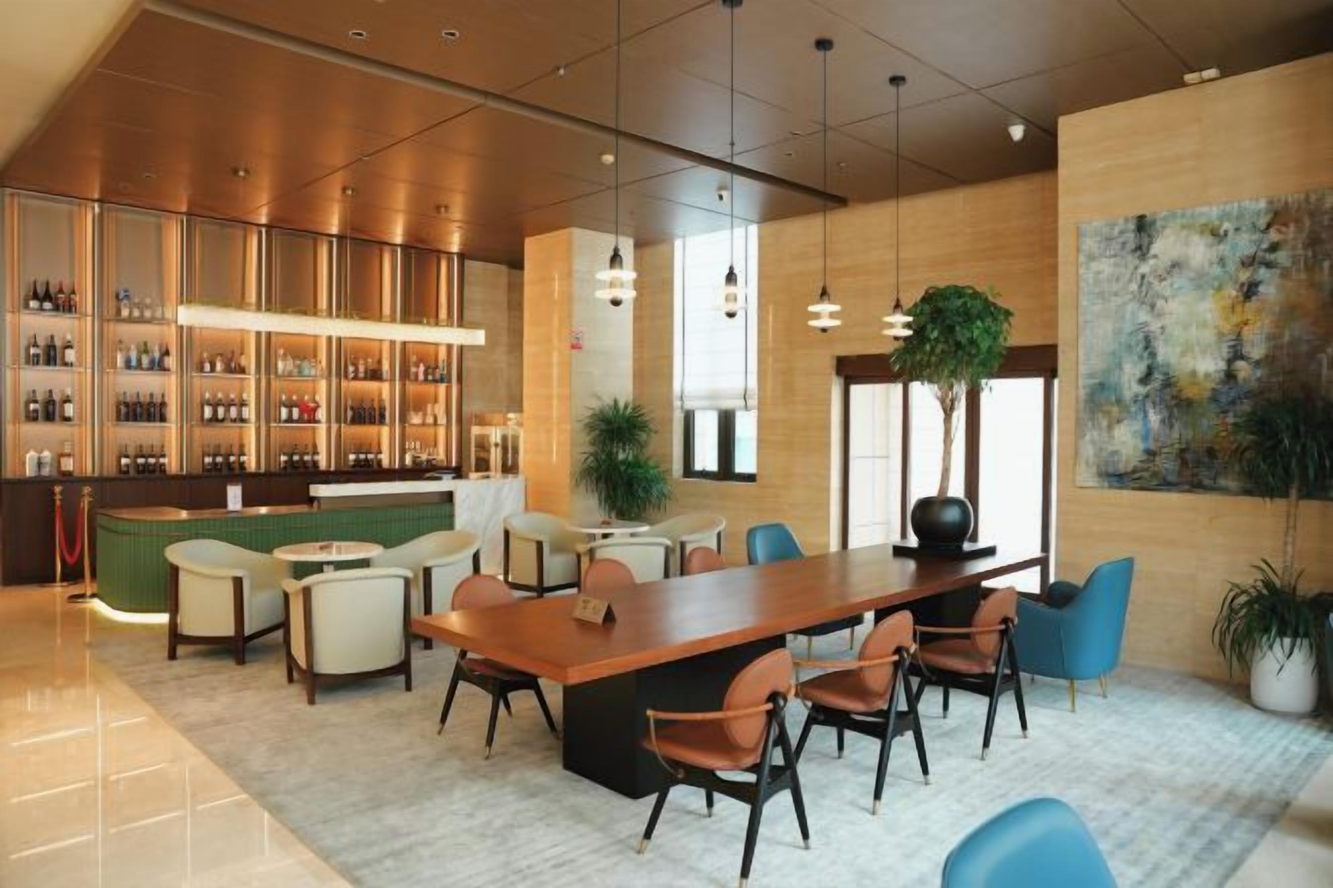 A modern bar area with a long counter, seating for guests, and a large abstract painting on the wall.
