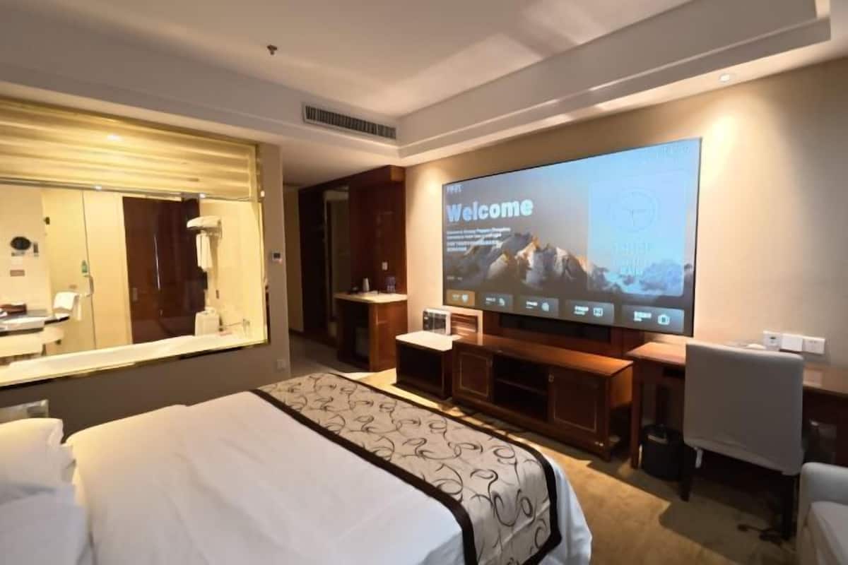 Ein Hotelzimmer mit einem großen Bett, einem Fernseher, der eine Willkommensnachricht zeigt, einem Spiegel und einer kleinen Sitzecke.