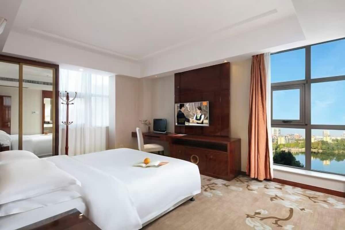 Ein Hotelzimmer mit einem großen Bett, einem Fernseher, einem Schreibtisch und Seeblick.