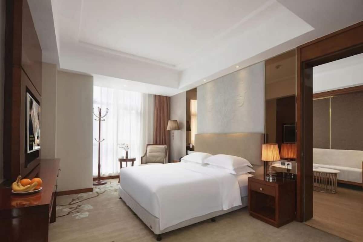 Ein Hotelzimmer mit einem großen Bett, Nachttischen, einem Sessel, einem Schreibtisch und einem Fenster mit Vorhängen.