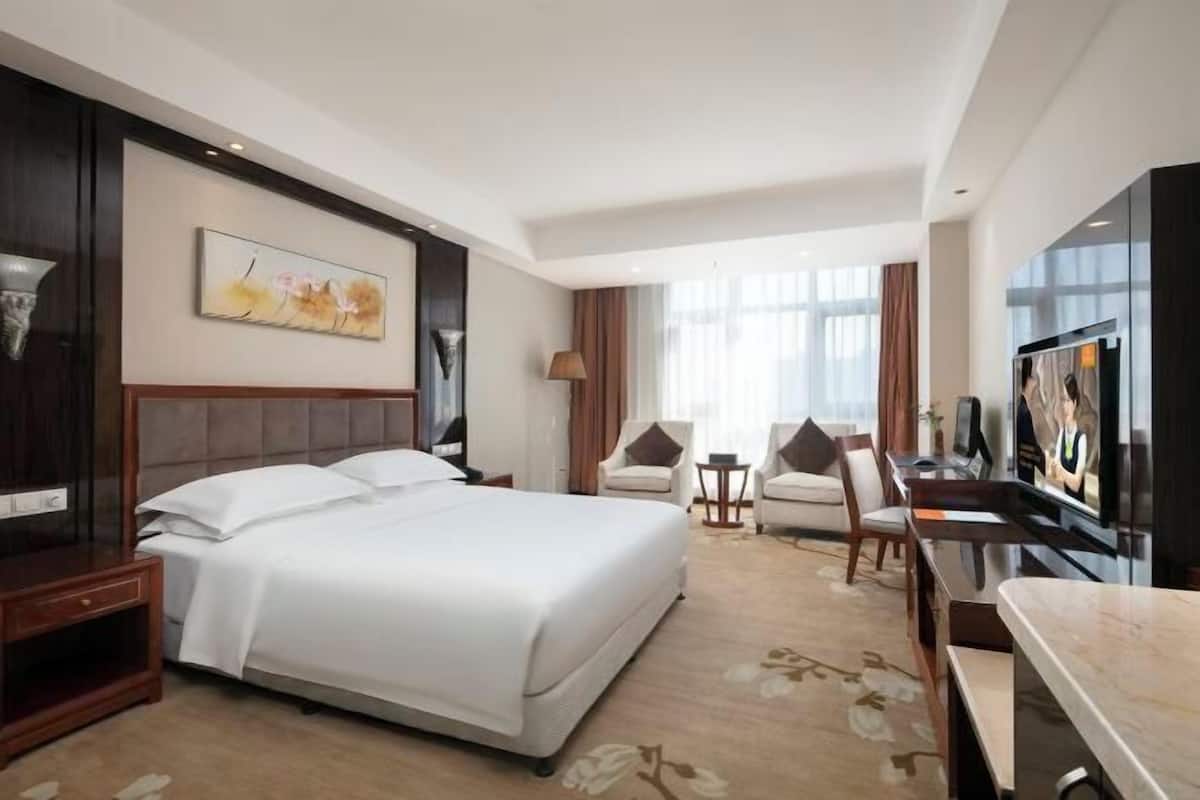 Ein Hotelzimmer mit einem großen Bett, einem Fernseher, einem Schreibtisch und einem Sessel.