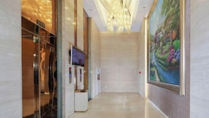 A hallway with a chandelier, a painting, and a television screen.