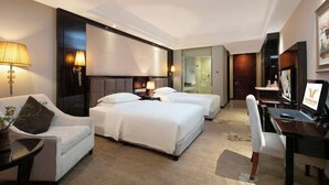 A hotel room with two beds, a desk, a chair, a lamp, and a television.