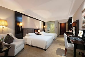 Ein Hotelzimmer mit zwei Betten, einem Schreibtisch, einem Stuhl, einer Lampe und einem Fernseher.