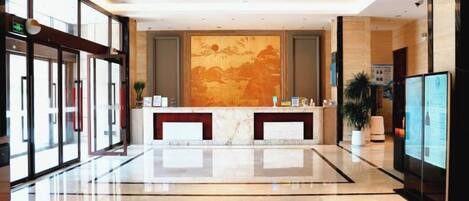 A hotel lobby with a reception desk, glass doors, a large wall mural, and a polished floor.