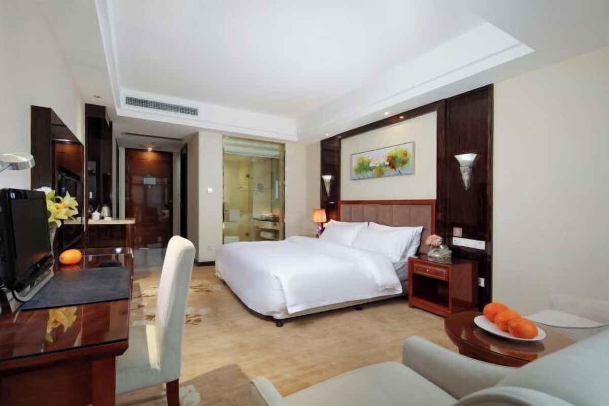 A hotel room with a bed, bedside table, lamp, and a desk with a chair.