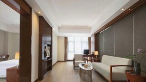 A hotel room with a bed, a sofa, a TV, a desk, and a coffee table.