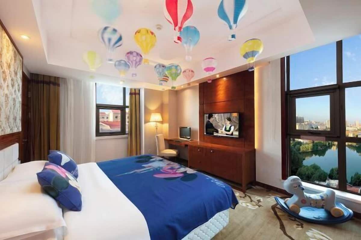 Ein Hotelzimmer mit einem großen Bett, einem Fernseher, einem Schreibtisch und Blick auf eine Skyline durch große Fenster.