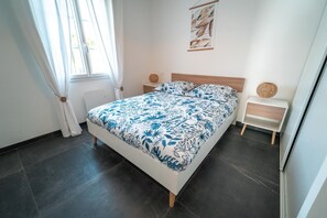 Ett sovrum med en säng, två sängbord, ett fönster med gardiner och ett konstverk som hänger på väggen.
