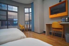 A hotel room with two beds, a desk, a chair, a TV, and a window with a view of buildings.
