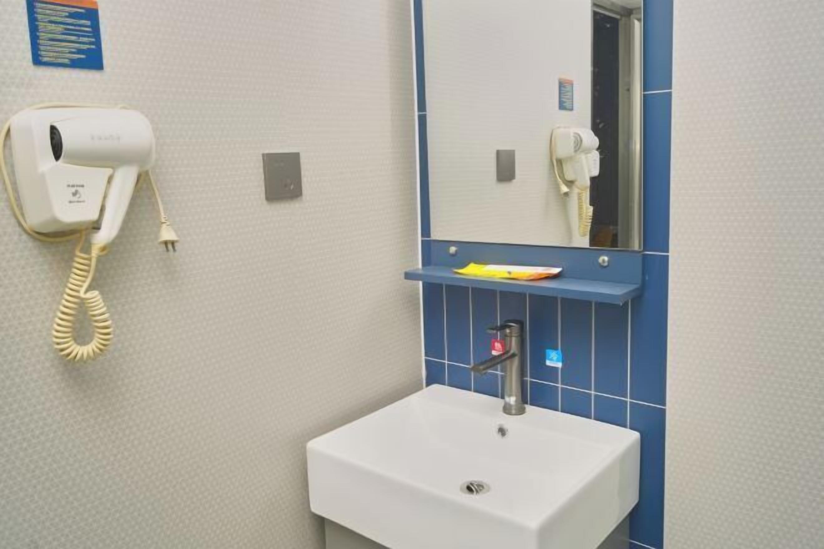 A bathroom with a white sink, a mirror, a hairdryer, and a shelf with toiletries.