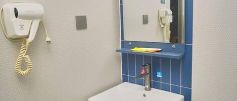 A bathroom with a white sink, a mirror, a hairdryer, and a shelf with toiletries.