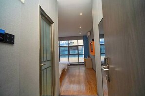 A hotel corridor with a wooden floor, a bed, and a window with a view of the outside.