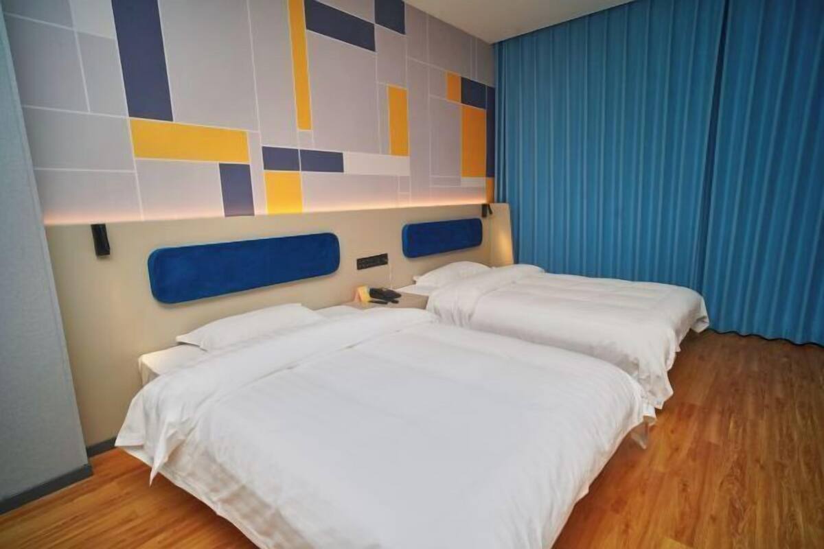 Une chambre d’hôtel avec deux lits, une tête de lit moderne et un rideau bleu.