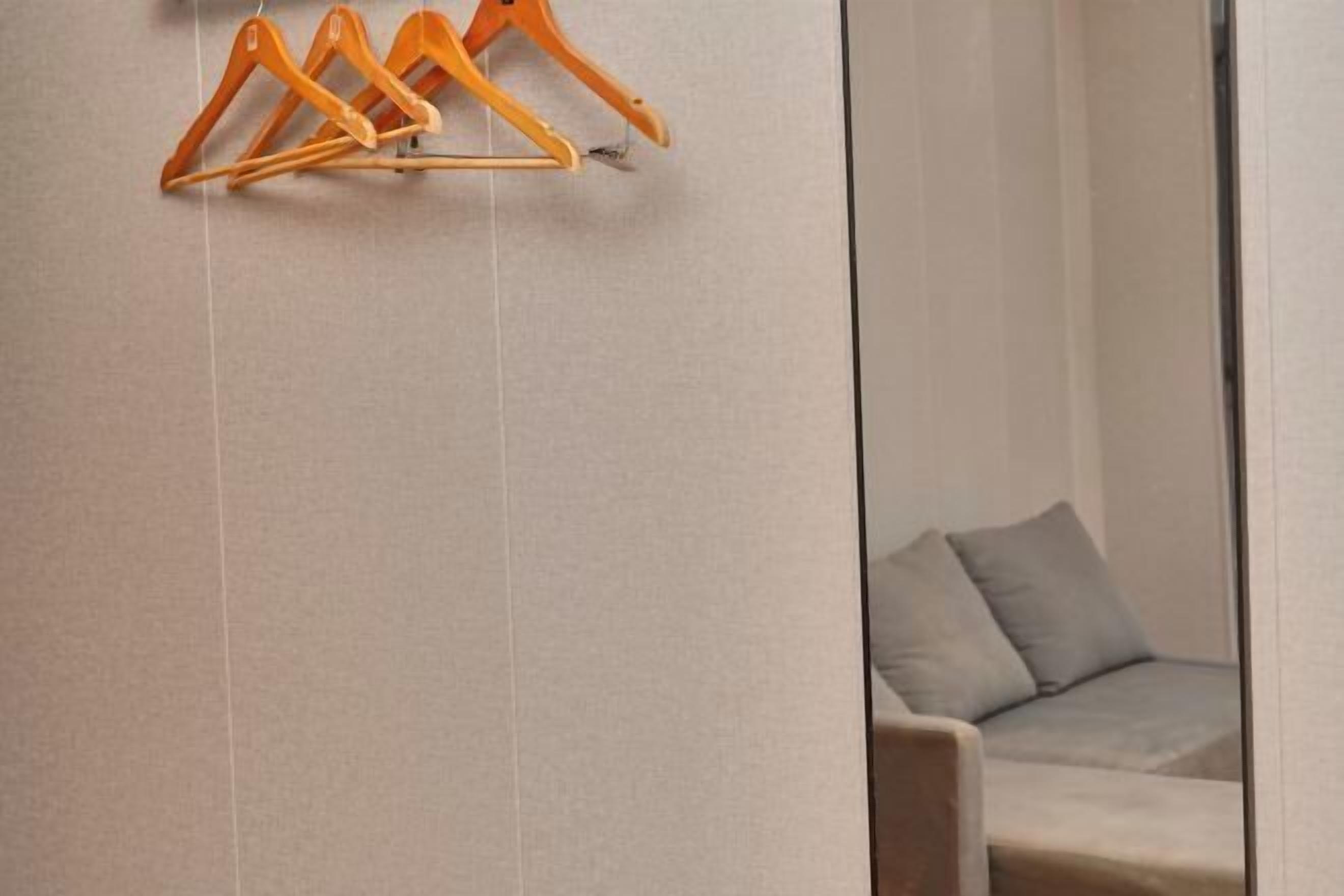 A room with a light-colored wall, a wooden hanger rack, and a grey sofa with cushions.