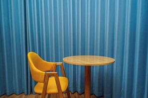 A room with a blue curtain backdrop, a yellow chair, and a round wooden table. - 7Days Inn Chain Hotel (Chongqing Bund International) (Chongqing)