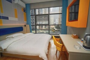 A hotel room with a bed, a desk, a chair, and a window with a city view.