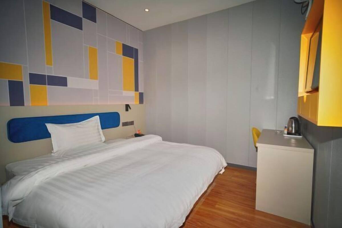 Une chambre d’hôtel avec un lit, une petite kitchenette et un mur orné de motifs géométriques.