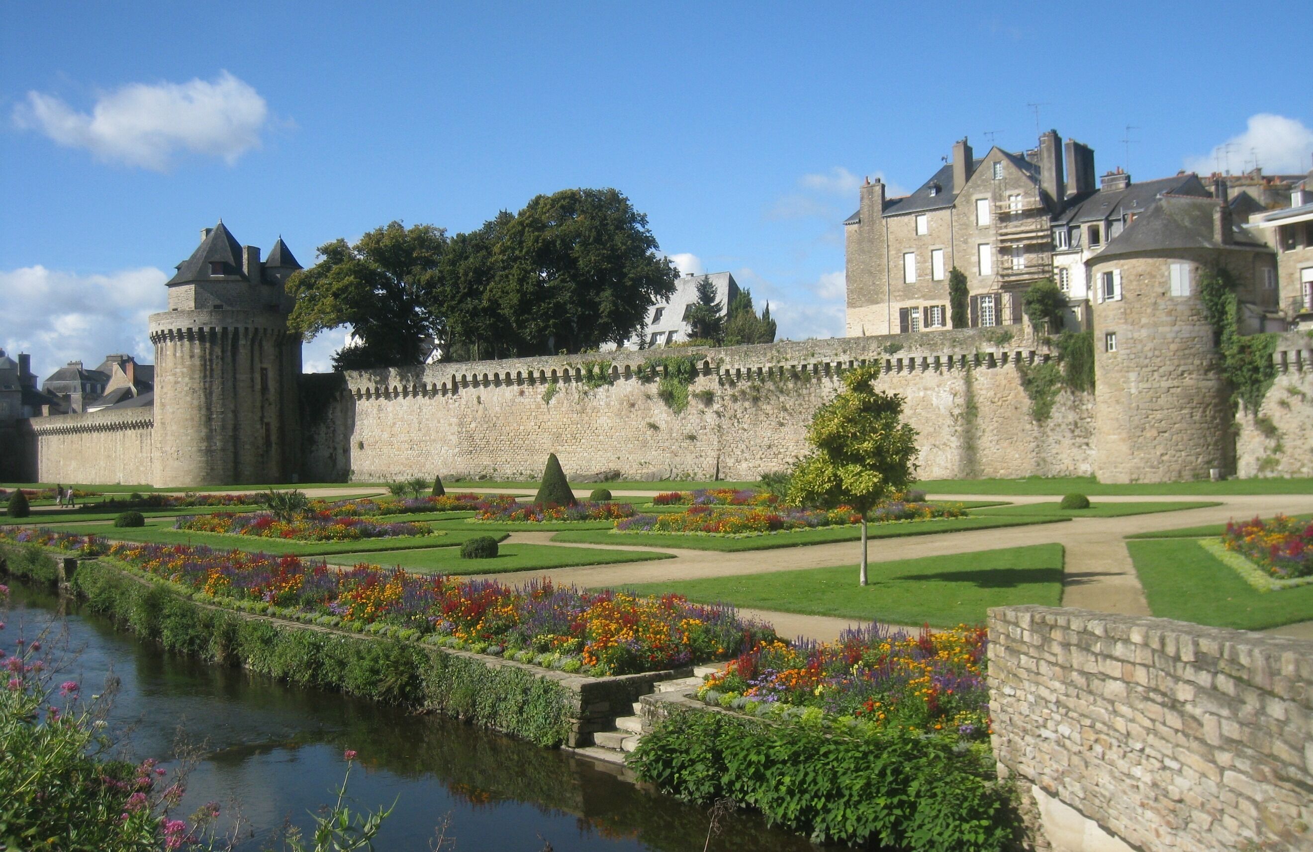 Un château historique, doté d’un fossé, entouré de jardins magnifiquement entretenus et surplombant un ciel dégagé.
