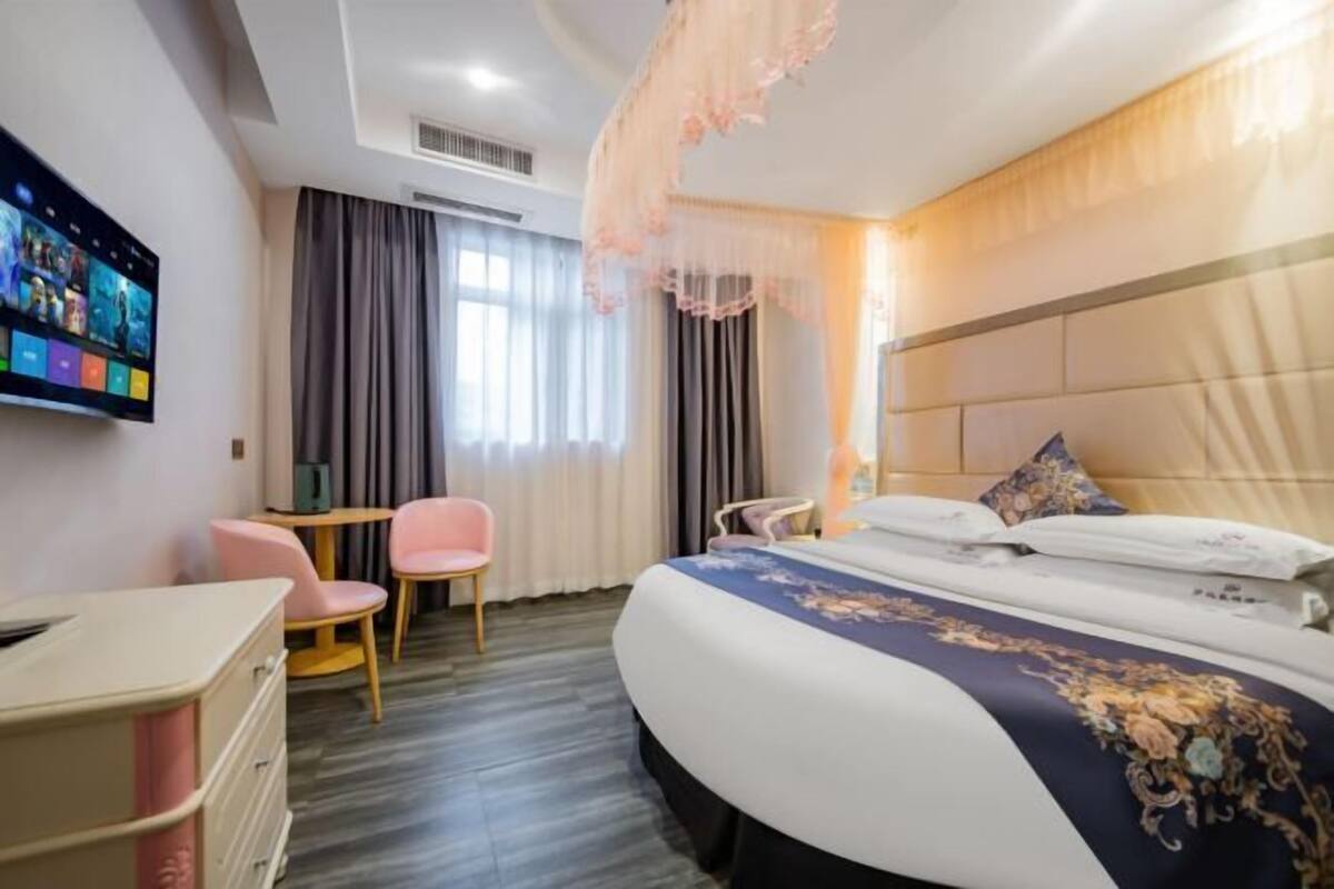 A hotel room with a bed, a desk, a chair, and a television on the wall.