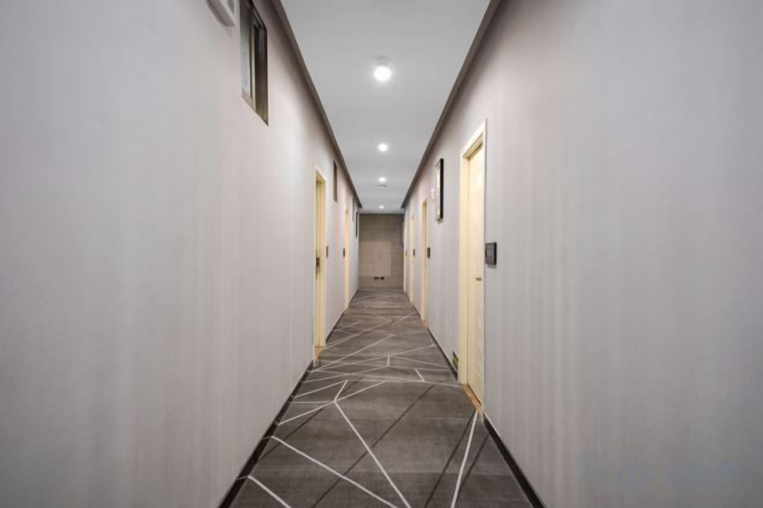 Un couloir d’hôtel avec des portes de part et d’autre, une moquette à motifs et un plafond doté d’un éclairage encastré.