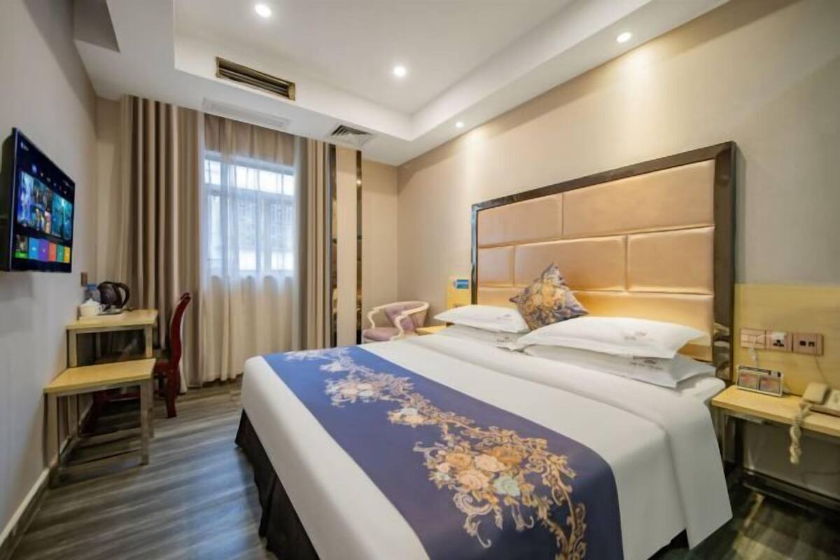 A hotel room with a bed, a desk, a chair, a TV, and a bedside table.