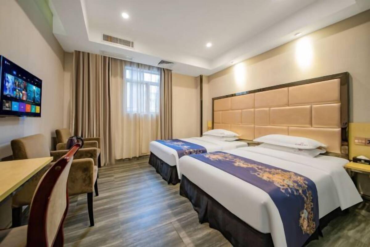 A hotel room with two beds, a TV, a desk, and a chair.