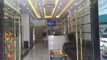 A hotel lobby with a reception desk, seating area, and a television screen.