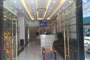 Un vestíbulo de hotel con una recepción, zona de estar y una pantalla de televisión.