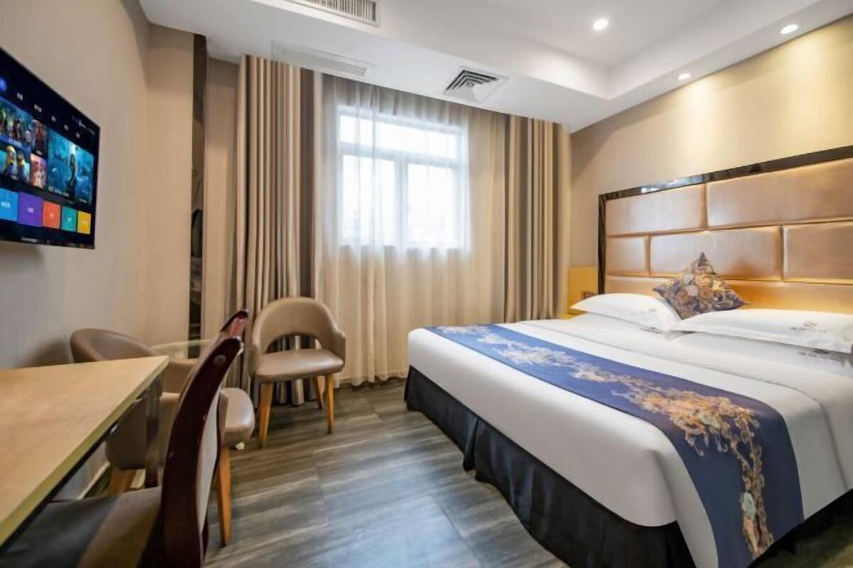 A hotel room with a bed, a desk, a chair, a TV, and a window with curtains.