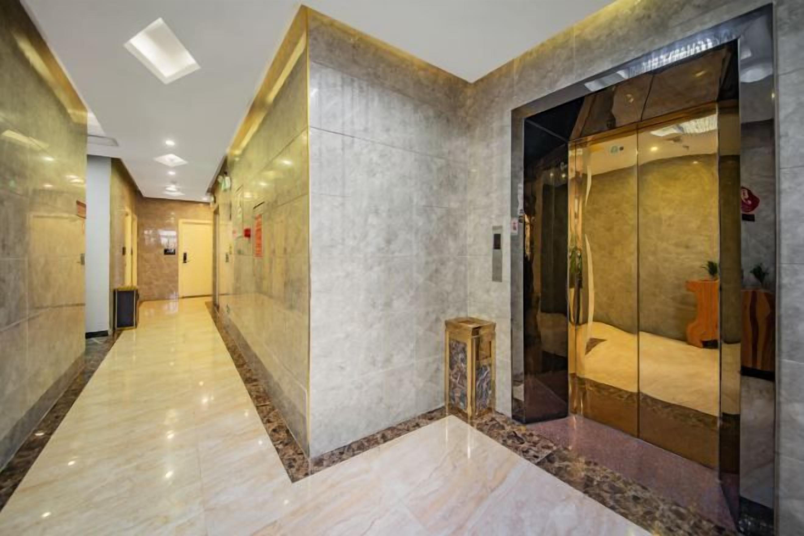 Un pasillo de hotel con piso de mármol, un ascensor de vidrio y un taburete de madera.