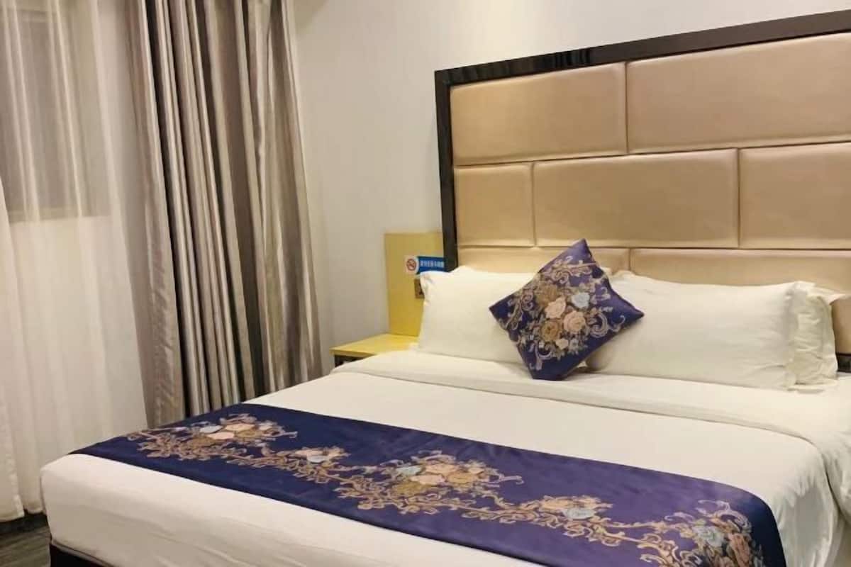 A hotel room with a bed, a headboard, a nightstand, and a curtain.