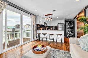 A modern kitchen with a central island, bar stools, and a built-in washer and dryer. - 1 BR Condo with Water Views + 2 Minute Walk to Beach (Carolina Beach)