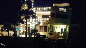 A multi-story building with balconies and outdoor lighting, parked cars in front, and palm trees. - #4, VRBO MAP PLACEMENT WRONG, CHECK GOOGLE MAP,LAS CONCHAS,1ST HOUSE, HEART ICON (Puerto Peñasco)
