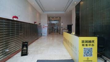 A hotel reception area with a reception desk, a signboard, and a glass door leading to the interior.