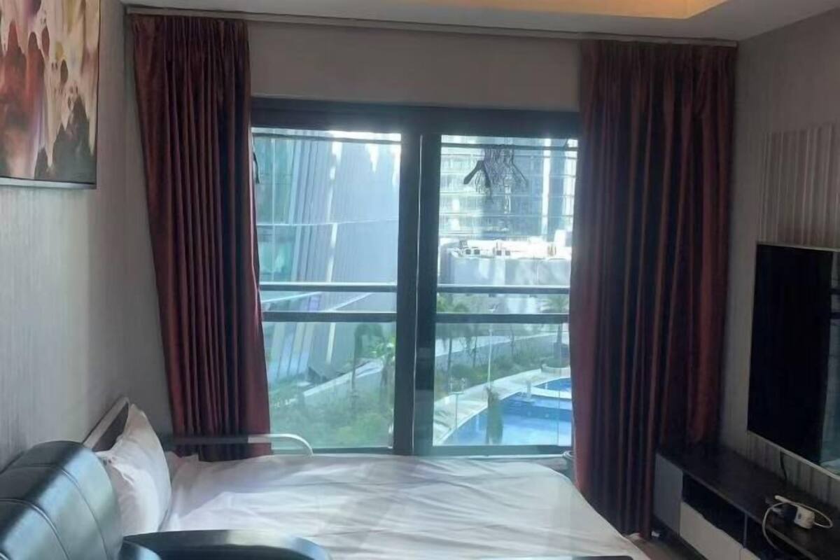 A hotel room with a bed, a television, and a large window with curtains.