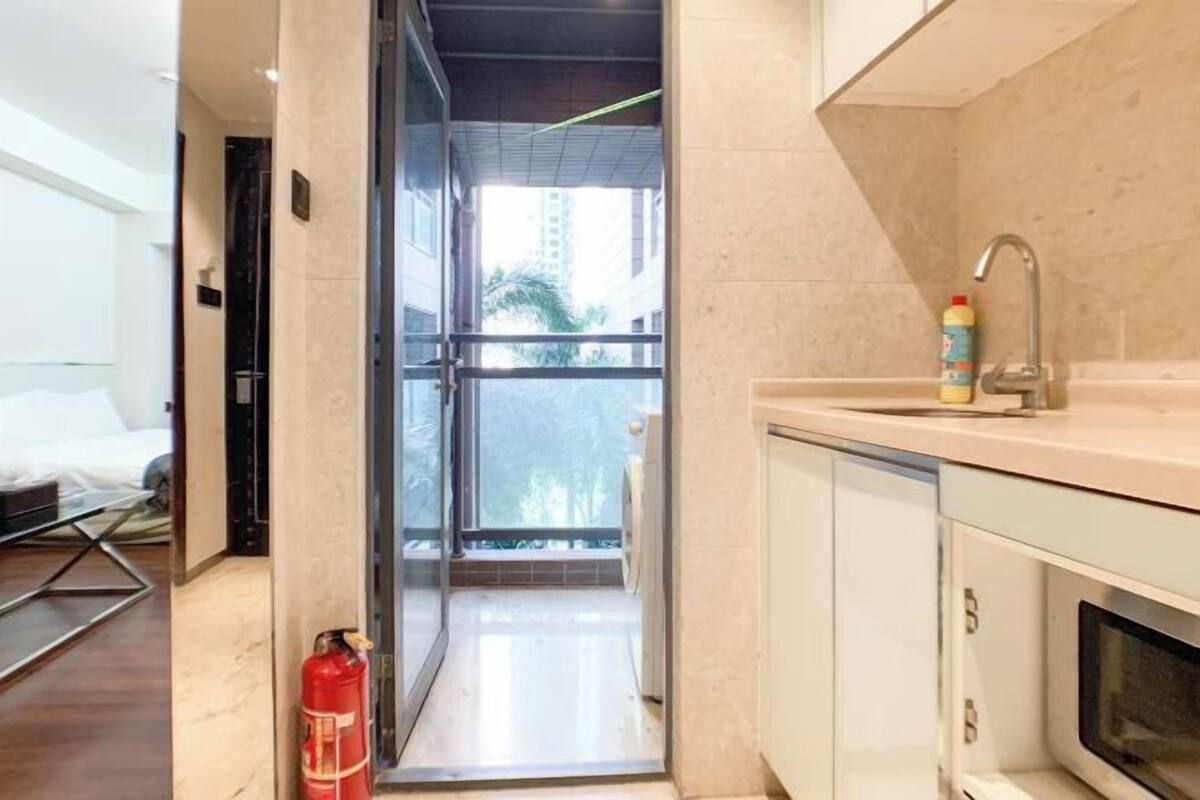 A modern hotel room with a glass door leading to a balcony, a kitchen area with a microwave, and a fire extinguisher.