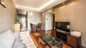 Una sala moderna con un sofá, una mesa de centro de vidrio, un televisor de pantalla plana y un comedor con sillas y una mesa.
