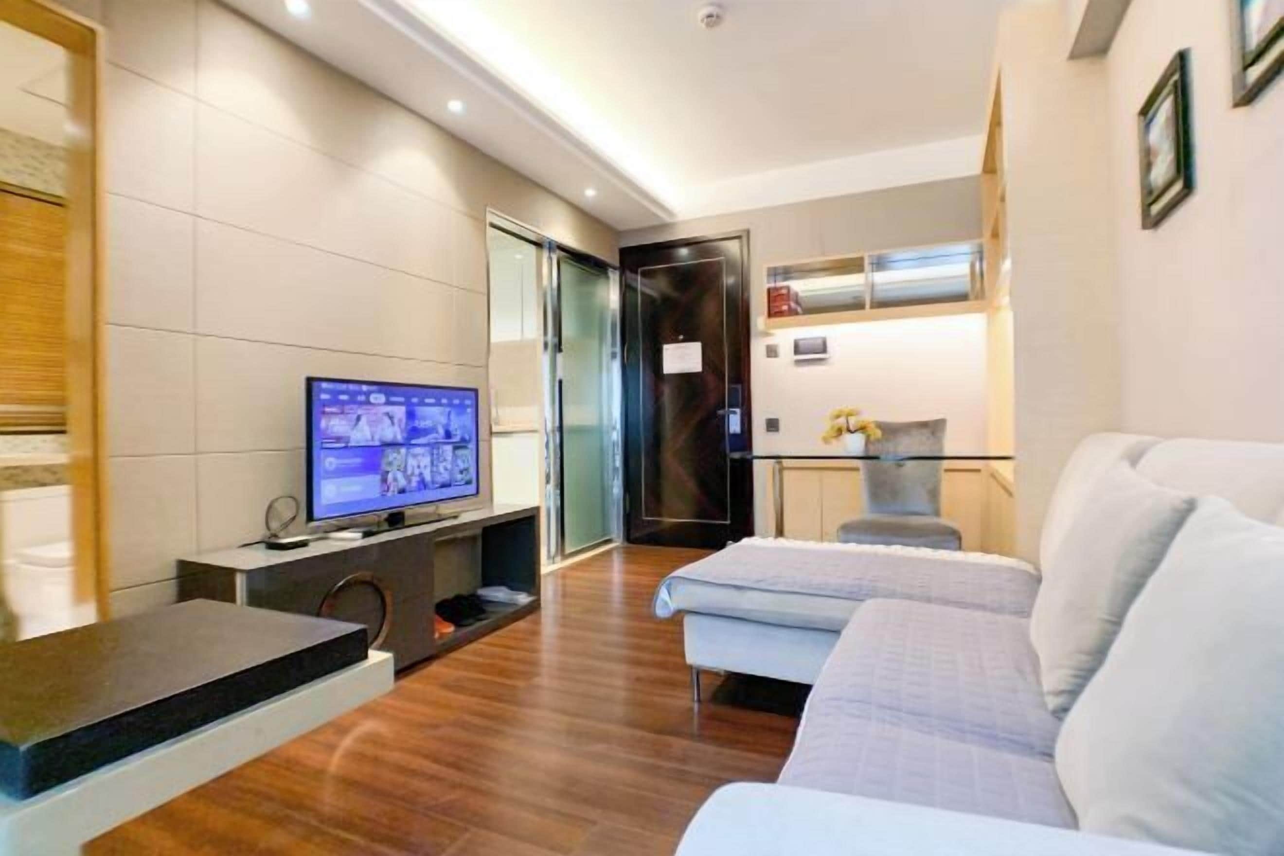 Ein modernes Hotelzimmer mit Flachbildfernseher, einer Couch, einem kleinen Tisch und einem Schrank.
