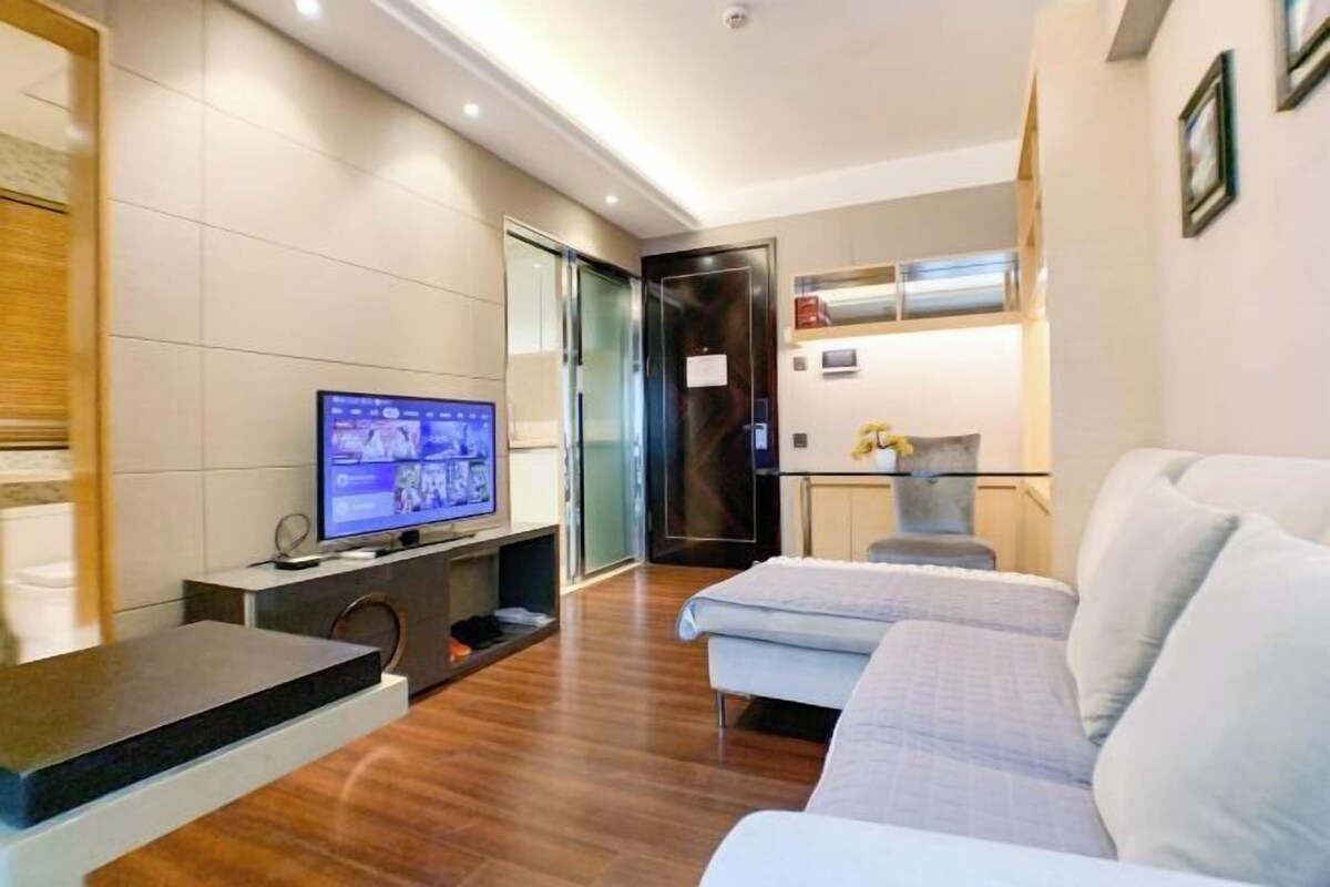 A modern hotel room with a flat-screen TV, a sofa, a small table, and a cabinet.