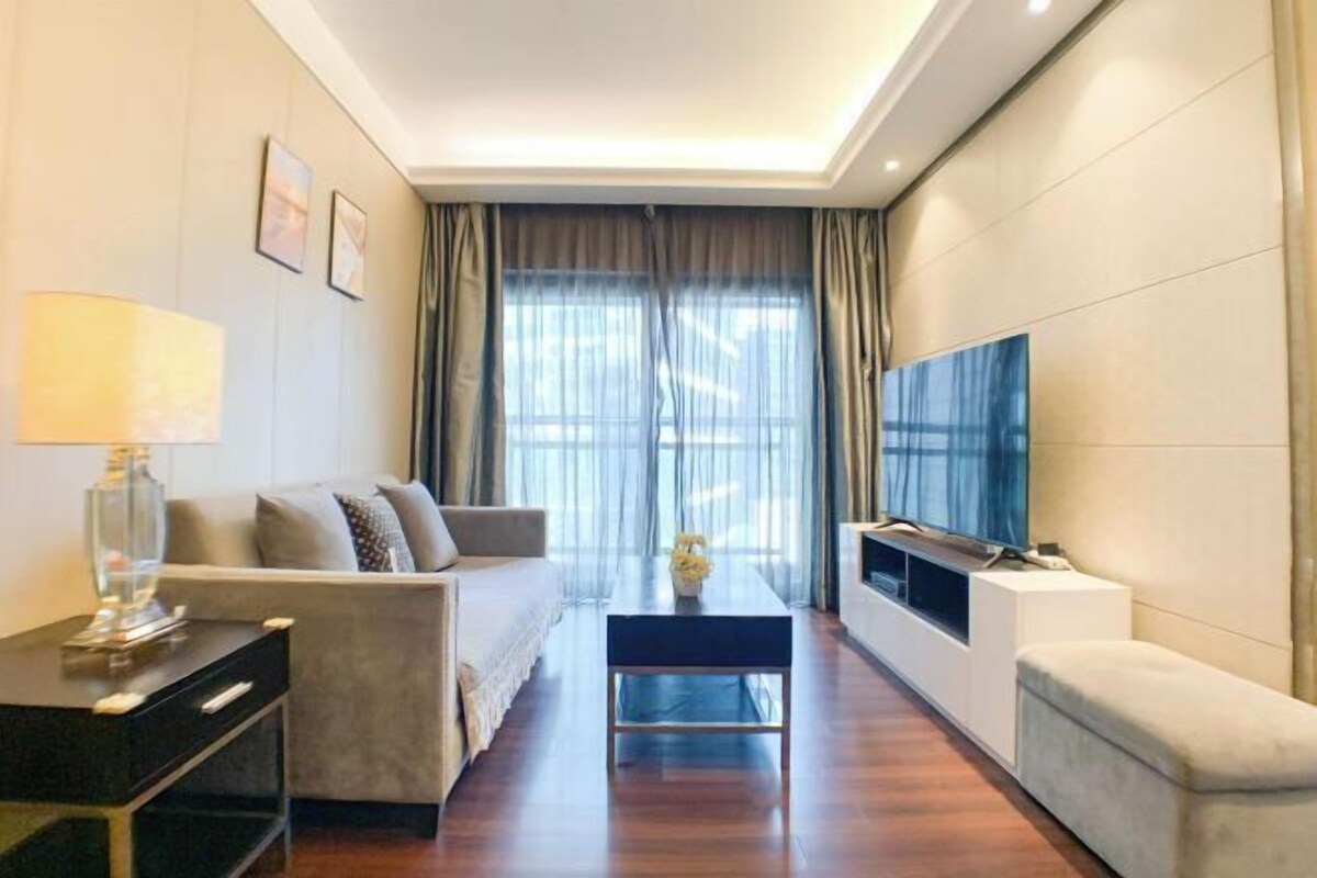 A modern living room with a sofa, coffee table, TV, and a large window with curtains.