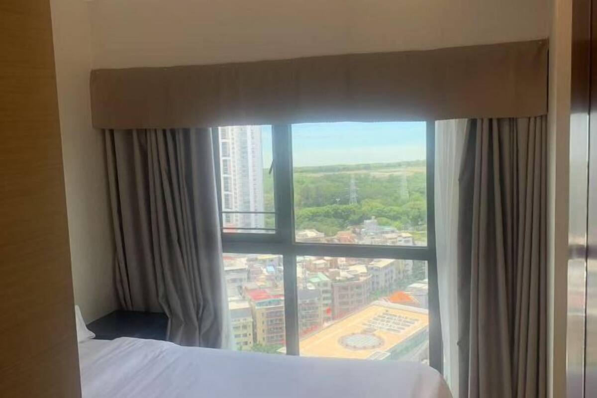 A hotel room with a large window, a bed, and curtains.