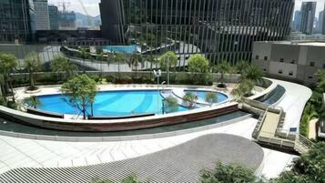 A rooftop swimming pool with a circular design, surrounded by greenery and modern buildings in the background.