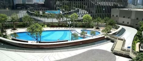 A rooftop swimming pool with a circular design, surrounded by greenery and modern buildings in the background.
