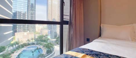 A hotel room with a large window offering a view of high-rise buildings and a pool.