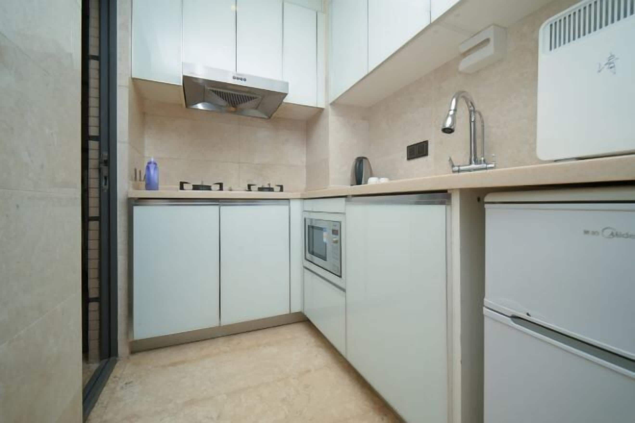 A compact kitchen with white cabinets, a built-in microwave, and a small refrigerator.