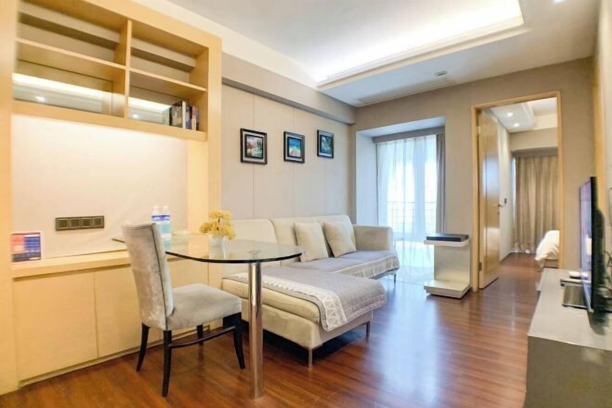 A modern living room with a glass table, a sofa, a chair, and a built-in shelving unit.