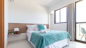 Una camera d'albergo moderna con un letto grande, un comodino con una lampada e vista all'esterno tramite un'ampia finestra.